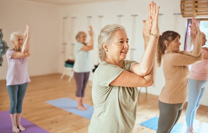 Grupo de mujeres mayores practicando yoga en una sala iluminada, realizando posturas de estiramiento y meditación en colchonetas de colores.